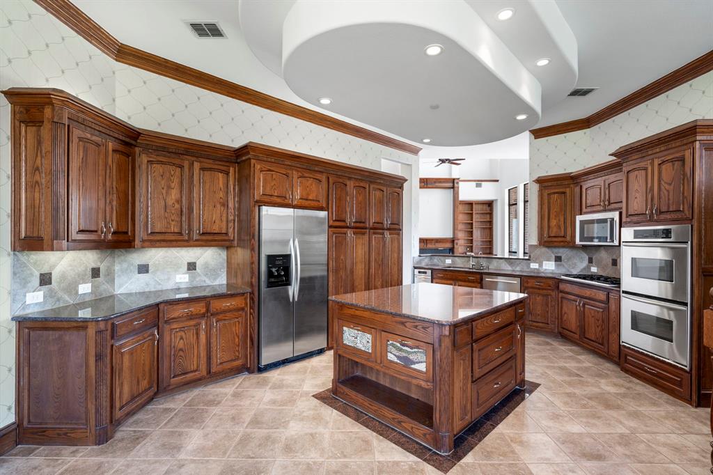 1000 Saddlebrook Drive Lucas, TX 75002 - Photo 18 of 39 Kitchen featuring Custom cabinets with pull out drawers, separate walk in pantry,, tasteful backsplash, dark stone counters, wallpapered walls, and stainless steel appliances