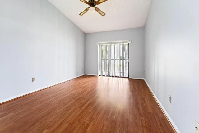 an empty room with wooden floor fan and windows