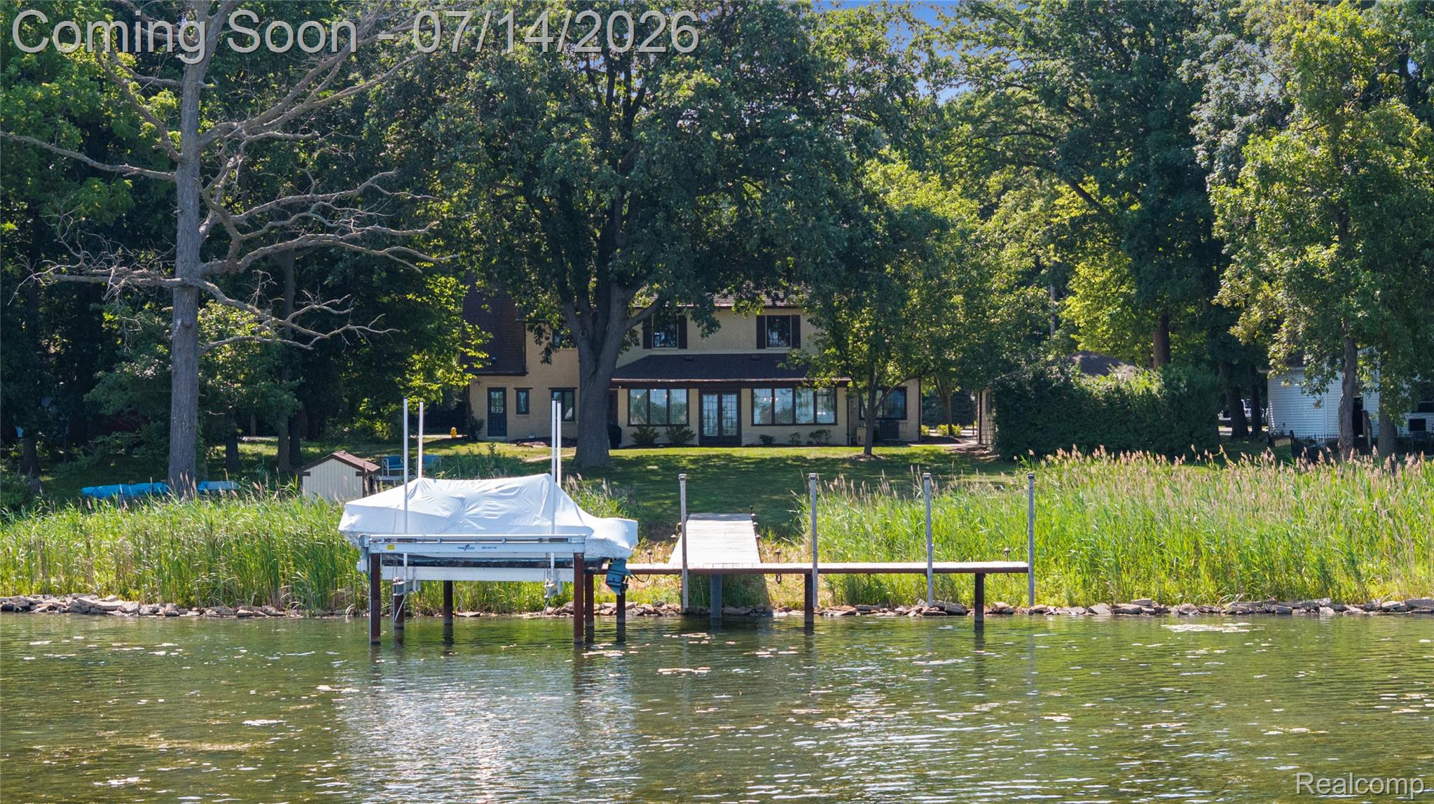 18460 Meridian Road Grosse Ile, MI 48138 - Photo 47 of 50 Waterfront property featuring a private dock with a boat lift, a spacious lawn leading to the water's edge, and a two-story residence with a large sunroom