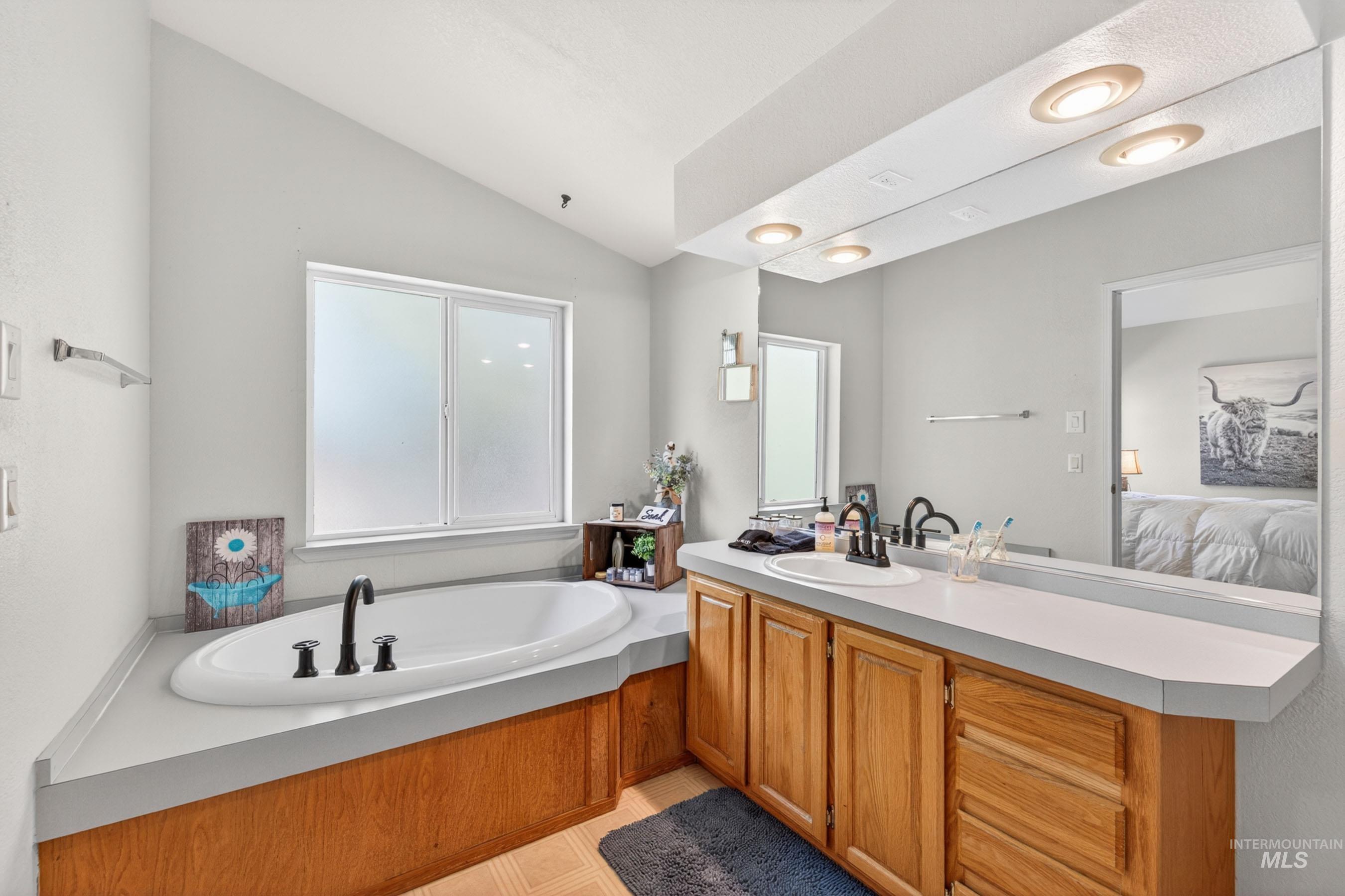 151 Cow Creek Road Lucile, ID 83542 - Photo 25 of 50 Bathroom featuring a built-in soaking tub with black fixtures, a double vanity with wood-finish cabinetry, and a large wall-mounted mirror
