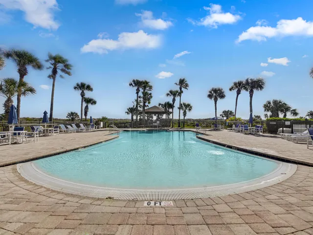 a view of a swimming pool with a lawn chairs under palm trees