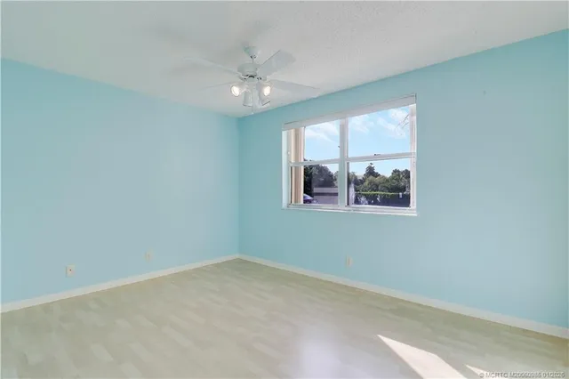 an empty room with chandelier fan and windows