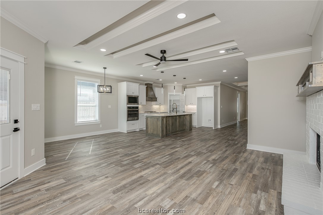2908 GOLDBERG Drive Bryan, TX 77808 - Photo 16 of 44 View of the family room into the kitchen, decorative cove lighting, ceiling fan with lite kit, can lights, gas fireplace, and wood mantle, floating shelves, pop up ceilings and vinyl flooring.