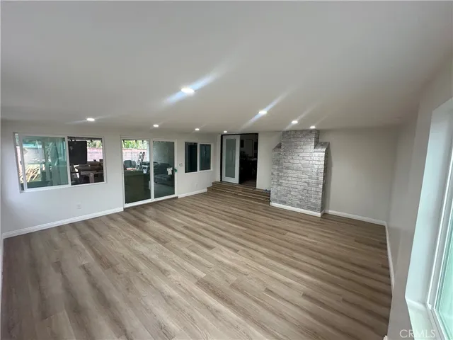 a view of an empty room with wooden floor and a kitchen