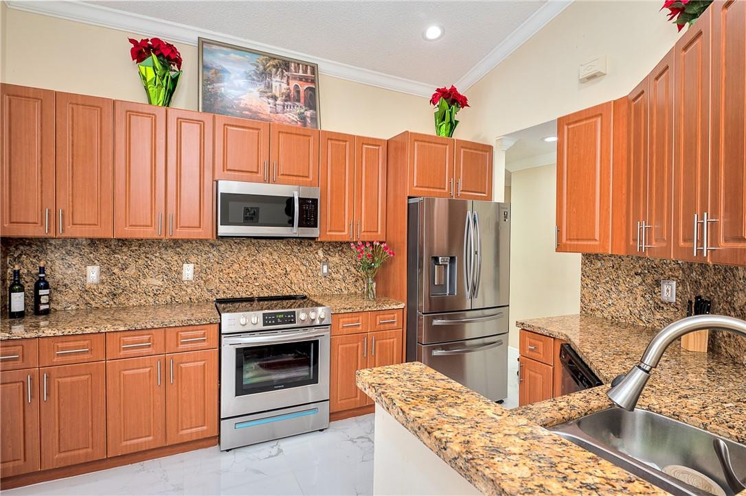 833 Falling Water Road Weston, FL 33326 - Photo 9 of 32 a kitchen with granite countertop wooden cabinets a stove top oven and refrigerator
