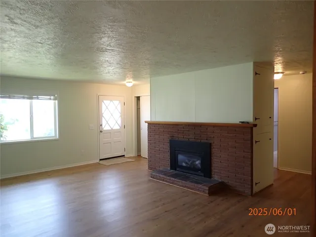 an empty room with wooden floor fireplace and windows