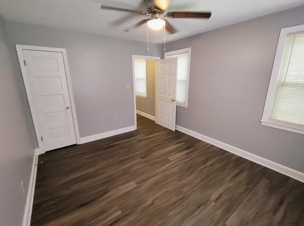 an empty room with wooden floor fan and windows