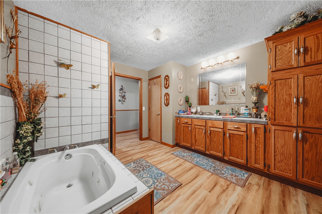 21587 West Hickory Flat Road Springdale, AR 72764 - Photo 26 of 45 Spacious primary bathroom with a jetted soaking tub, long vanity, abundant cabinetry, and wood flooring.
