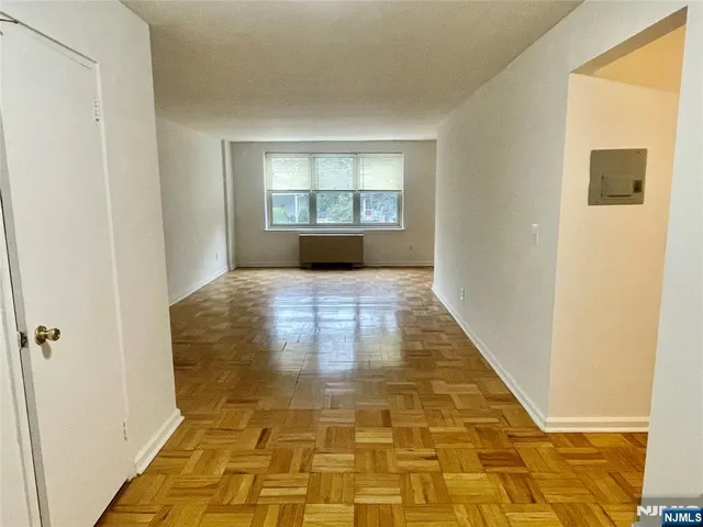 a view of a hallway to an empty room with wooden floor and a window