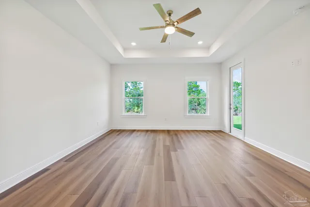 an empty room with wooden floor windows and fan
