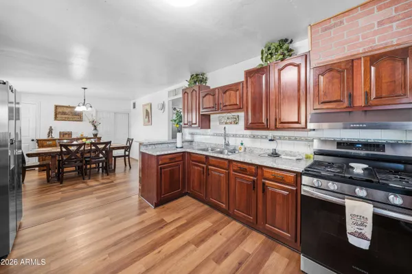 a kitchen with stainless steel appliances granite countertop a stove top oven a sink a dining table and chairs with wooden floor