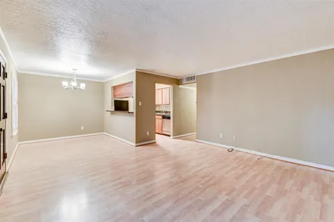 a view of an empty room with wooden floor and a kitchen