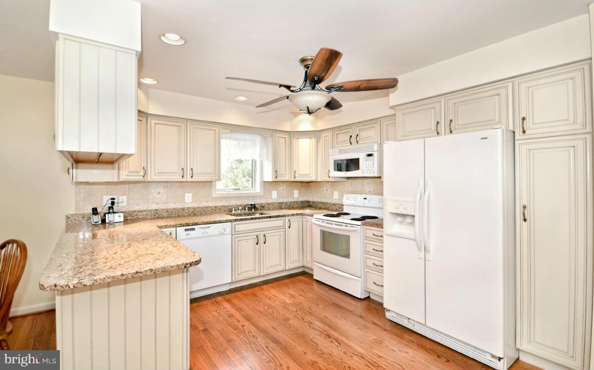 13912 Glen High Road Baldwin, MD 21013 - Photo 22 of 28 a kitchen with granite countertop a refrigerator a sink dishwasher a stove and white cabinets with wooden floor