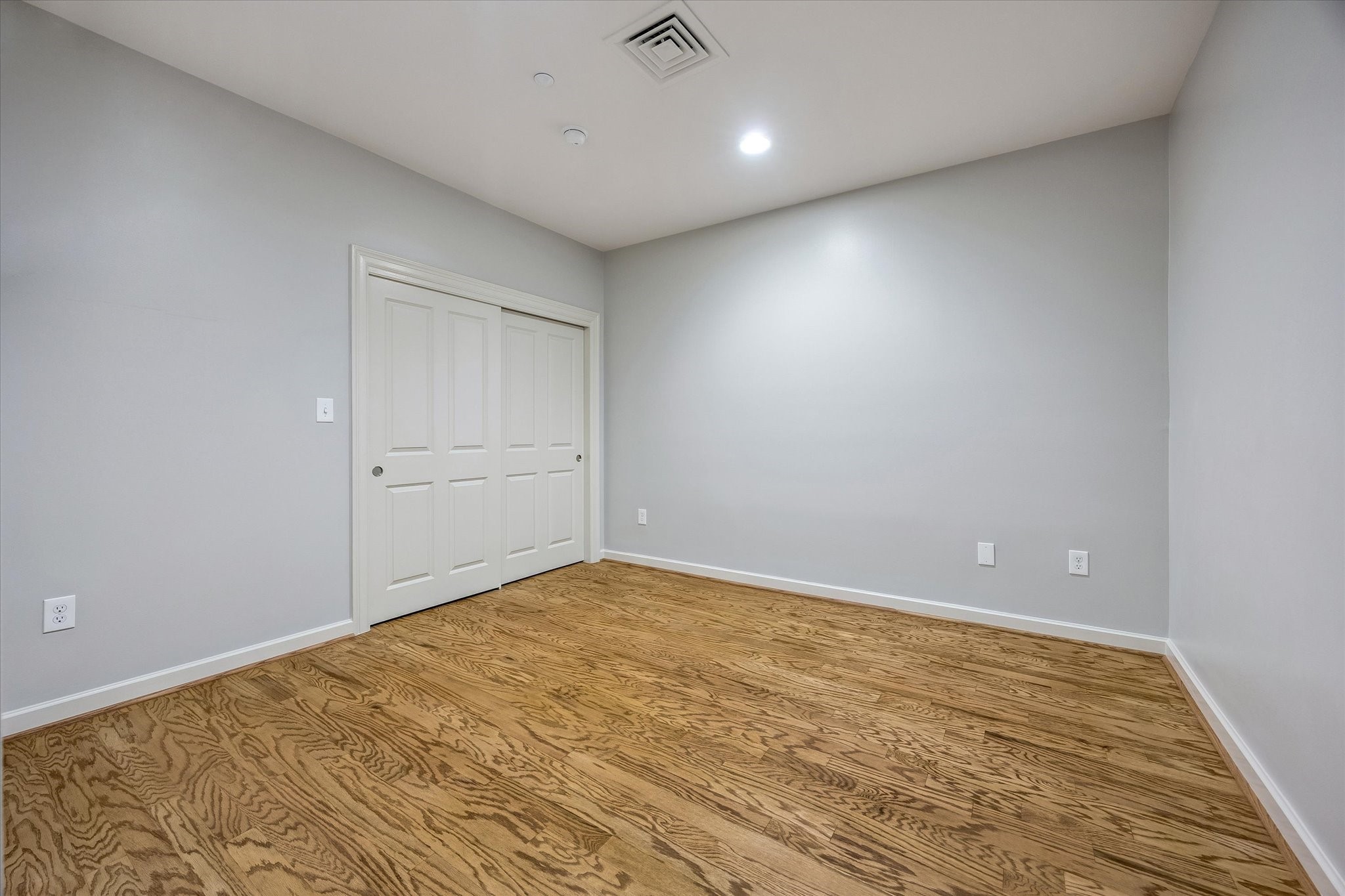 914 Main Street, Unit 910 Houston, TX 77002 - Photo 15 of 32 This is a simple, empty room with light gray walls, wood flooring, and a white sliding closet door. It features recessed lighting and has a clean, modern feel.