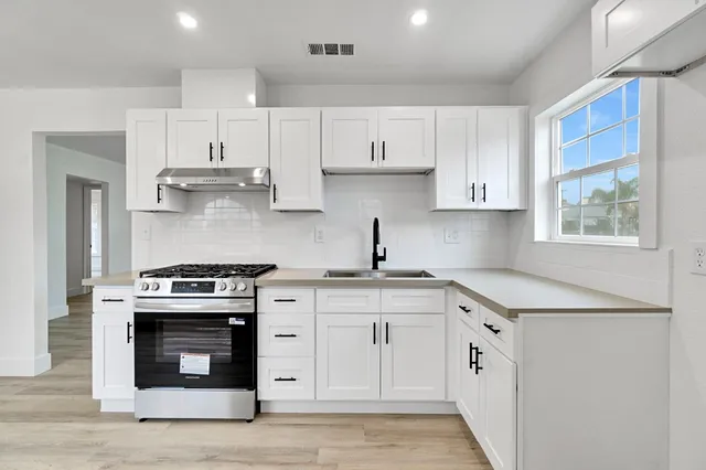 a kitchen with stainless steel appliances granite countertop a stove a sink and white cabinets