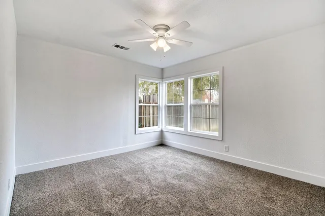 an empty room with chandelier fan and windows