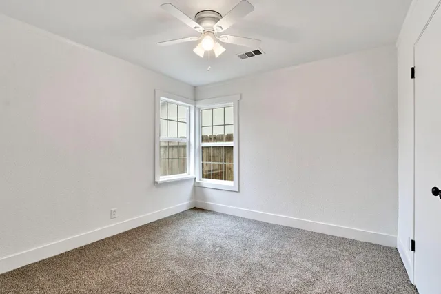 an empty room with windows and ceiling fan