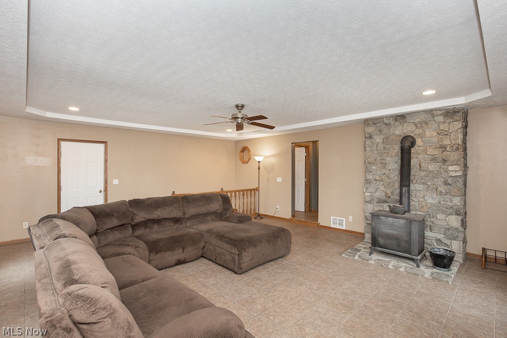 7484 Oberlin Road Elyria, OH 44035 - Photo 9 of 27 Tiled living room with a tray ceiling, ceiling fan, and a wood stove