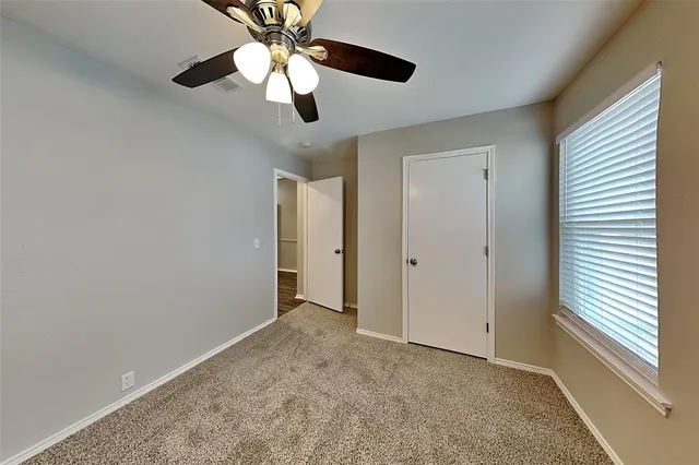 an empty room with chandelier fan and windows