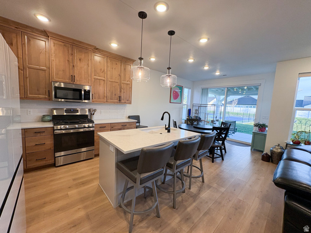 412 West 3025th Street South Logan, UT 84321 - Photo 19 of 34 Kitchen with stainless steel appliances, a center island with sink, a kitchen breakfast bar, decorative backsplash, and decorative light fixtures