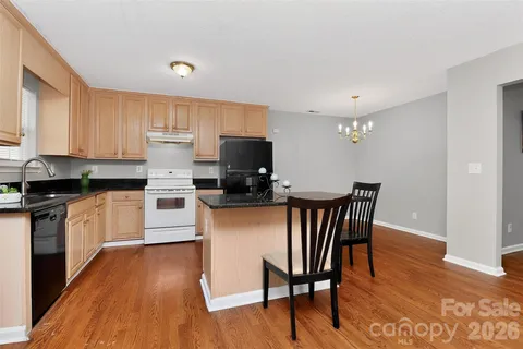 a kitchen with stainless steel appliances granite countertop a stove a sink a microwave a dining table and chairs with wooden floor