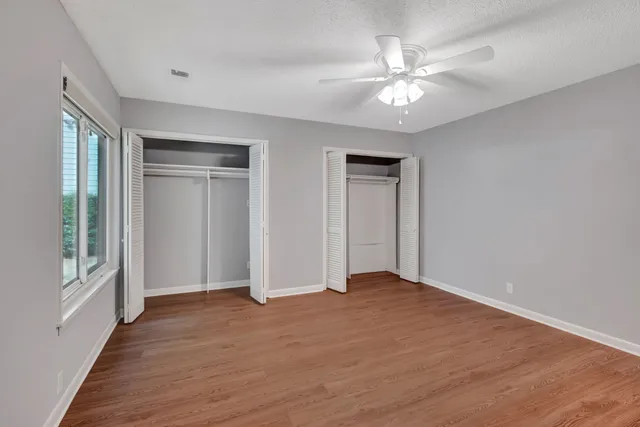 a view of an empty room with wooden floor and a ceiling fan