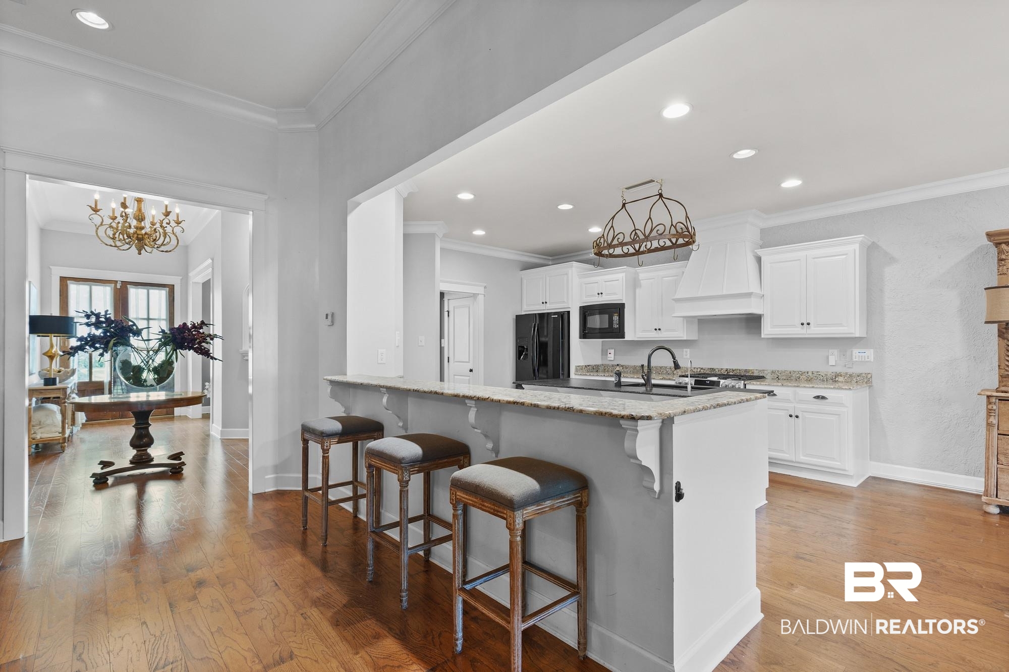 11261 Halcyon Loop Daphne, AL 36526 - Photo 9 of 41 Spacious kitchen featuring an expansive breakfast bar with a stone countertop, white cabinetry, integrated black appliances, and a decorative range hood