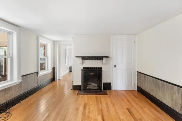 a view of an empty room with wooden floor fireplace and a window