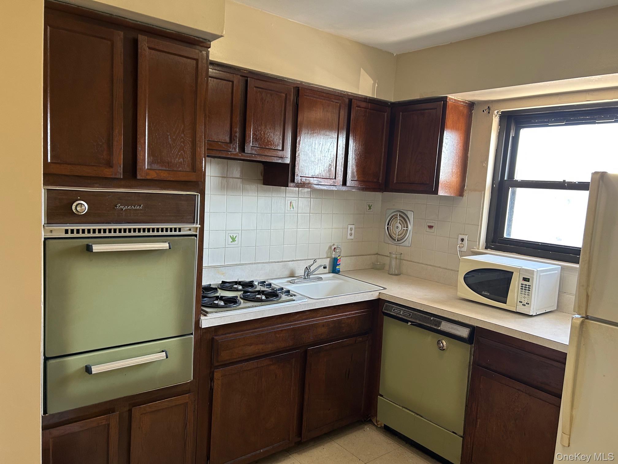 68 Sneden Place West, Unit 68 Spring Valley, NY 10977 - Photo 8 of 24 Kitchen with dark brown cabinets, white appliances, light countertops, a warming drawer, and decorative backsplash