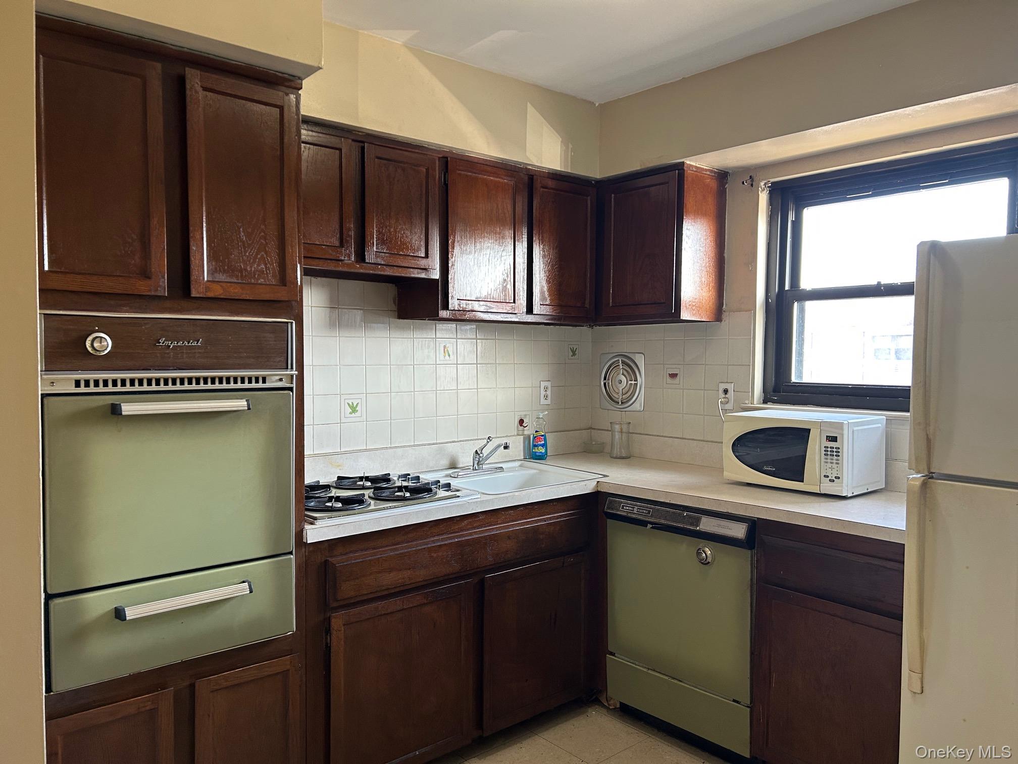 68 Sneden Place West, Unit 68 Spring Valley, NY 10977 - Photo 9 of 24 Kitchen featuring dark brown cabinetry, backsplash, white appliances, a warming drawer, and light countertops