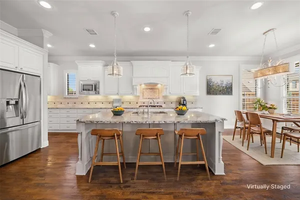a kitchen with kitchen island granite countertop a dining table chairs refrigerator and wooden cabinets