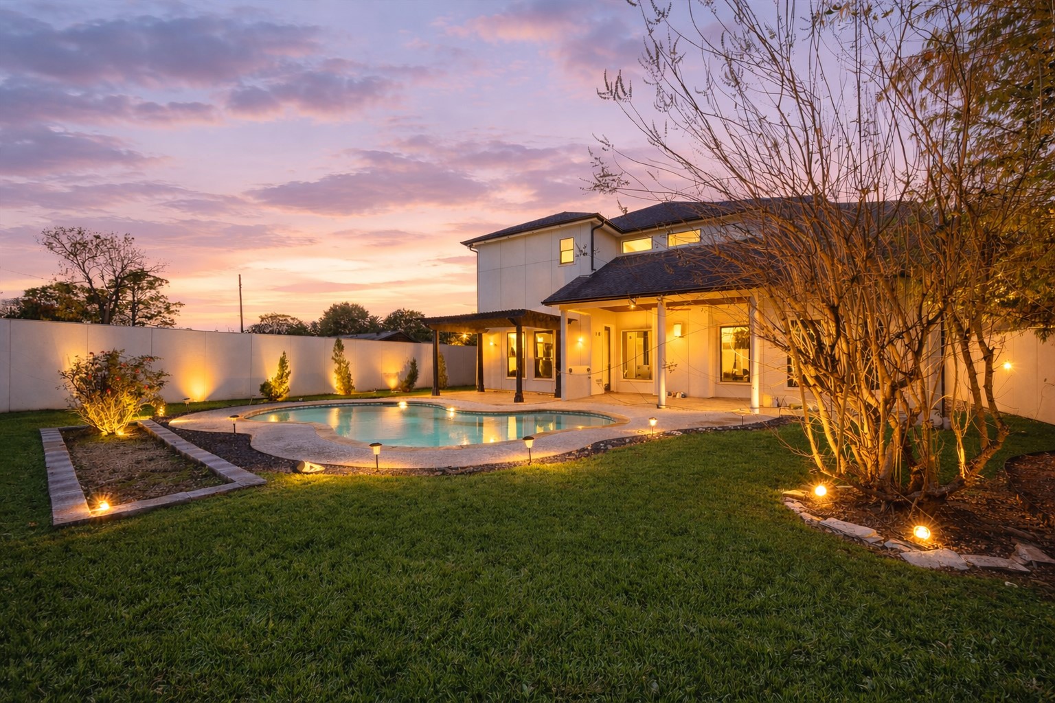 3942 Charleston Street Houston, TX 77021 - Photo 26 of 34 The backyard comes alive at dusk with a curved pool, landscape lighting, and a covered patio glowing from within. Privacy fencing and soft lighting create a clean, polished outdoor setting built for evenings at home or easy entertaining.