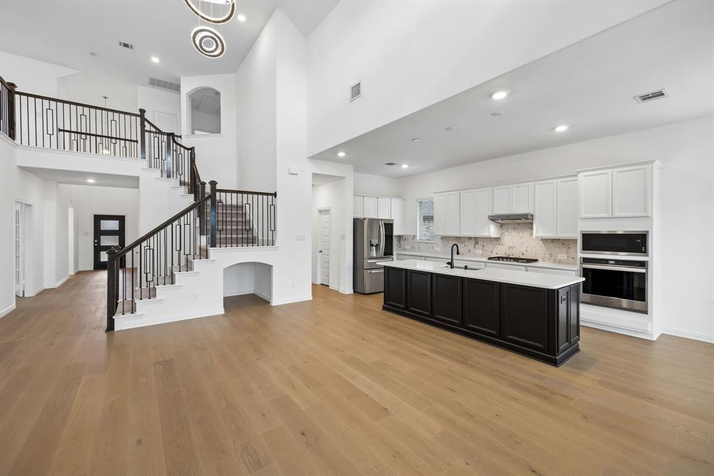 1303 Wheelwright Drive Forney, TX 75126 - Photo 2 of 39 Expansive open-concept living area featuring a two-story ceiling, wood-finish flooring, a contemporary kitchen with a large island, stainless steel appliances, and a grand staircase with decorative balusters