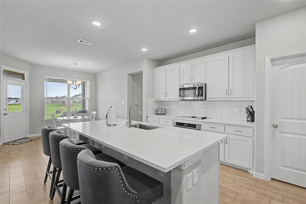 185 Chester Road Springtown, TX 76082 - Photo 16 of 40 Spacious kitchen featuring a large island with sink, quartz countertops, white shaker cabinetry, stainless steel appliances, and a herringbone tile backsplash