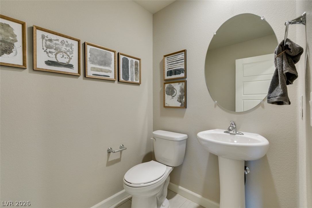 653 Pickled Pepper Place Henderson, NV 89011 - Photo 19 of 35 A well-appointed powder room features a classic pedestal sink and toilet, accented by a chic round mirror.