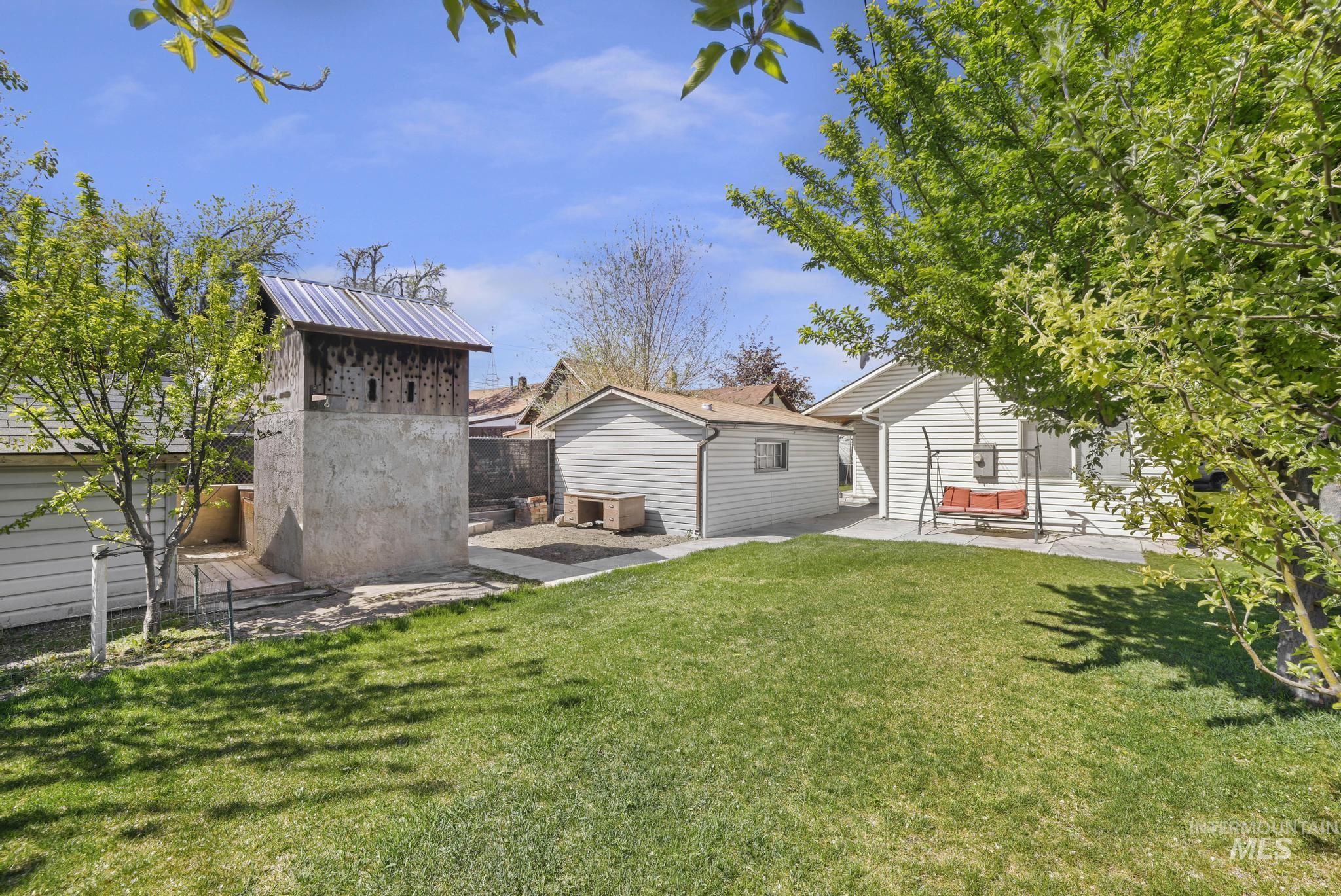 322 Jackson Street Twin Falls, ID 83301 - Photo 27 of 47 Expansive backyard featuring a manicured lawn, established trees, a detached garage, and a unique multi-level structure with a metal roof