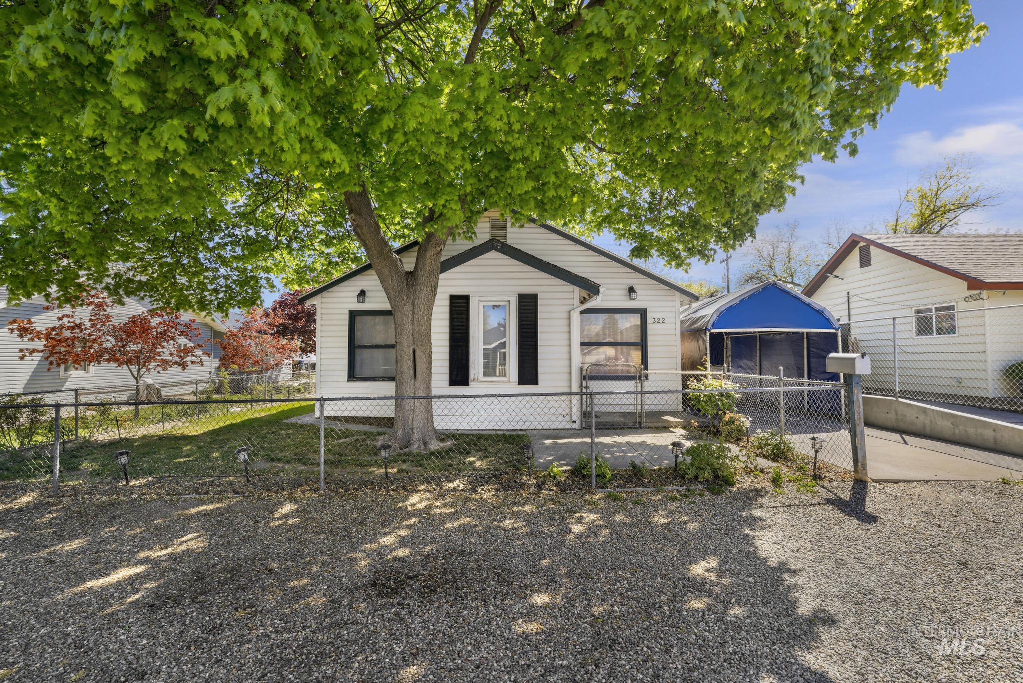 322 Jackson Street Twin Falls, ID 83301 - Photo 34 of 47 White siding residence featuring a large mature tree, dark window shutters, and a chain-link fence