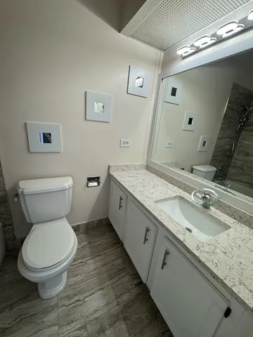 a bathroom with a granite countertop toilet a double vanity and a mirror