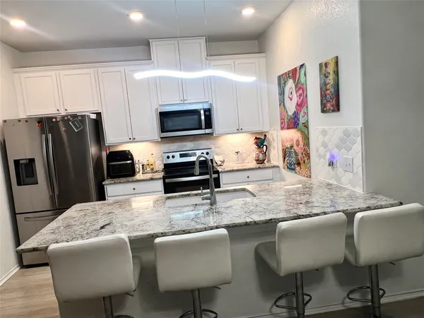 a kitchen with granite countertop a refrigerator a stove a sink a dining table and chairs with wooden floor