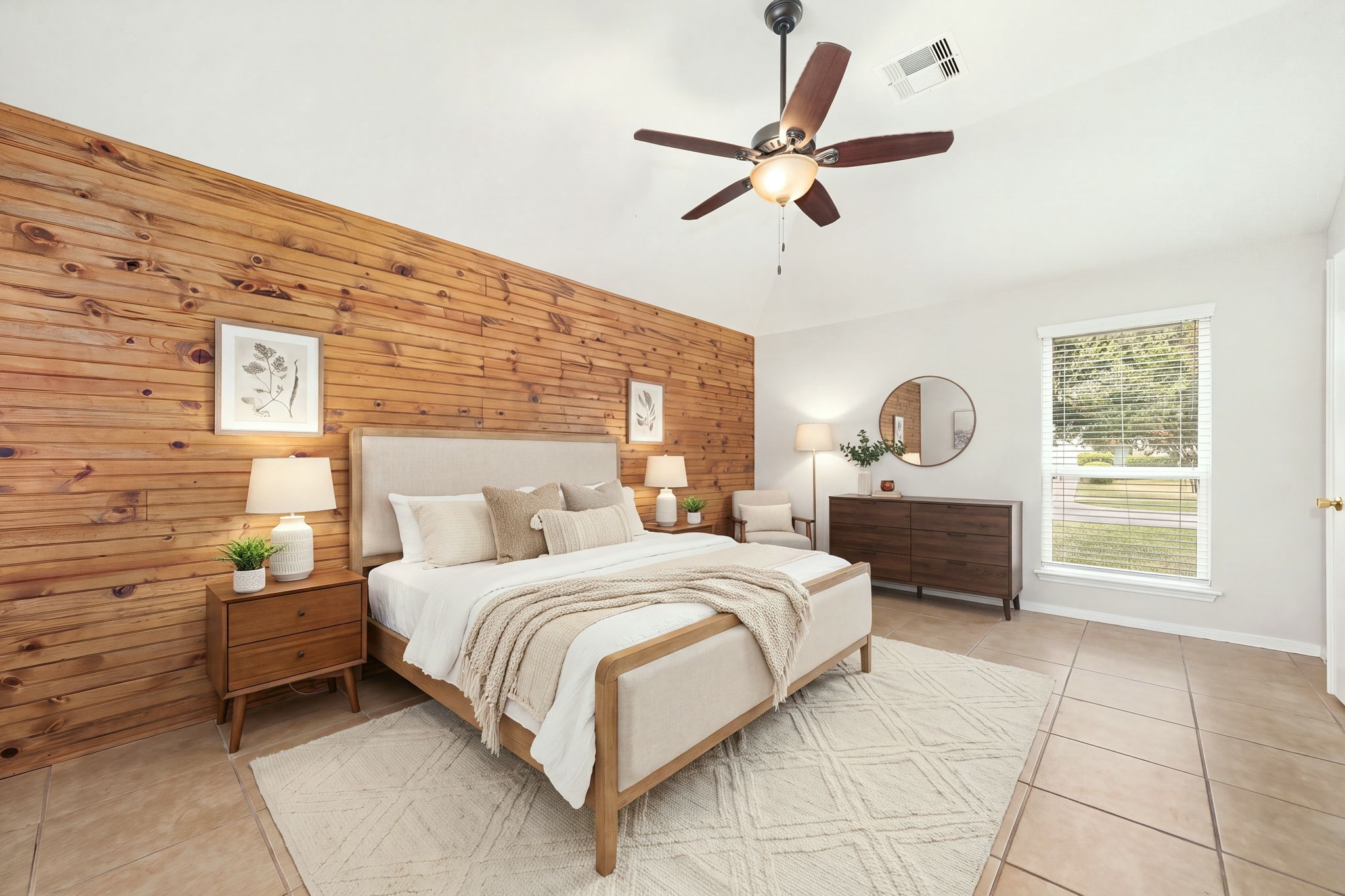 3102 Single Ridge Way Katy, TX 77493 - Photo 16 of 23 Spacious primary suite anchored by a beautiful, floor-to-ceiling wood plank accent wall that serves as a striking visual focal point. The bright room features vaulted ceilings, a central ceiling fan, and durable tile flooring, while a wide window allows for comfortable natural light. *Virtually Staged