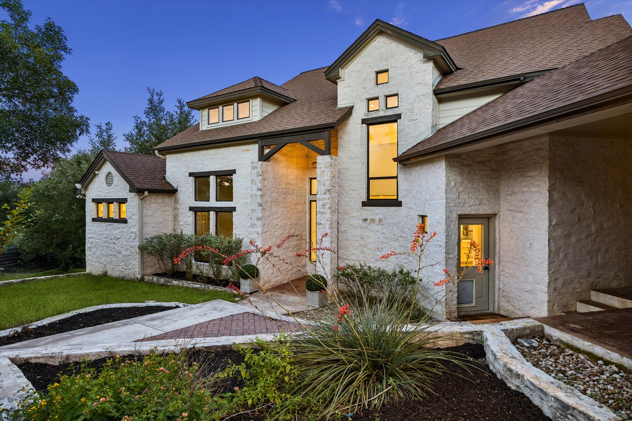 3719 Bee Creek Road Spicewood, TX 78669 - Photo 4 of 40 A stone-clad home featuring multiple gables and varied window designs, illuminated by evening lights.