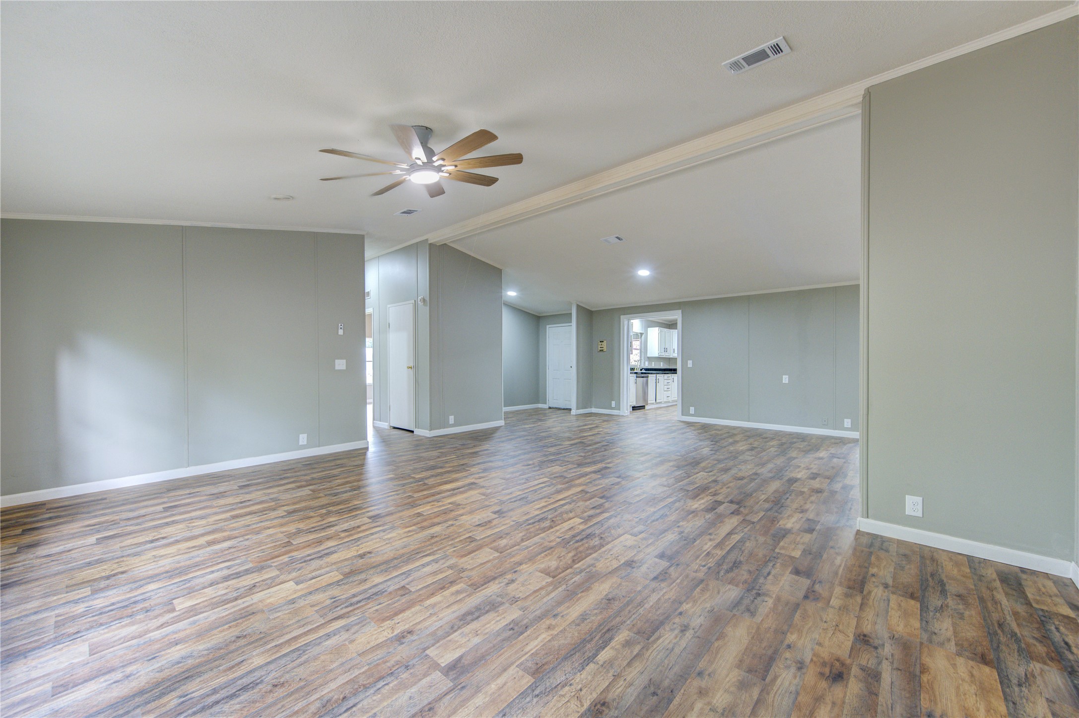 30226 Davis Street Magnolia, TX 77355 - Photo 10 of 50 This spacious living area features wood-style flooring, neutral-colored walls, and a ceiling fan. It offers an open layout with ample natural light and leads into the kitchen, creating a welcoming and versatile space.