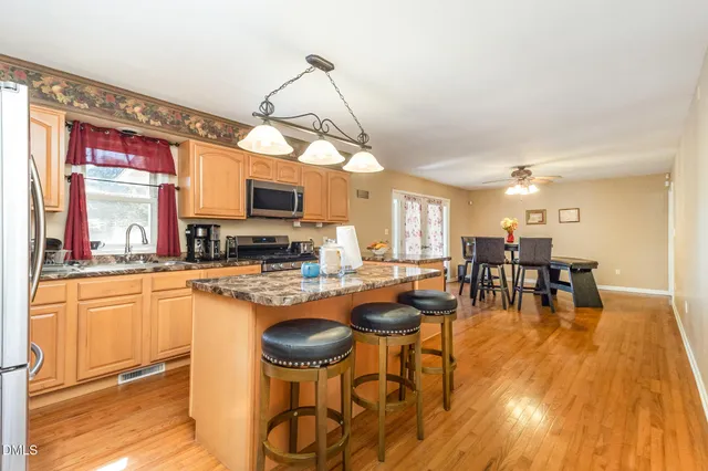 a kitchen with stainless steel appliances granite countertop a stove a refrigerator a kitchen island a dining table and chairs with wooden floor