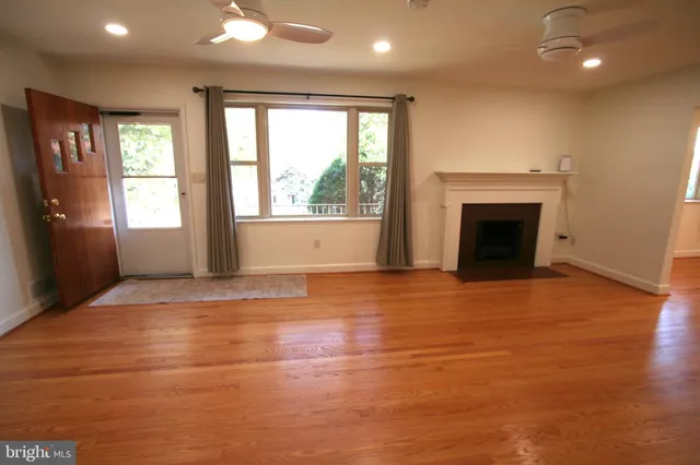 a view of an empty room with wooden floor fireplace and a window
