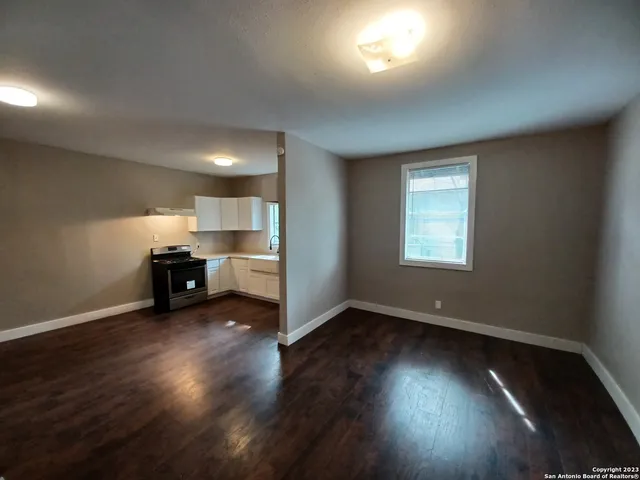 an empty room with wooden floor kitchen view and windows