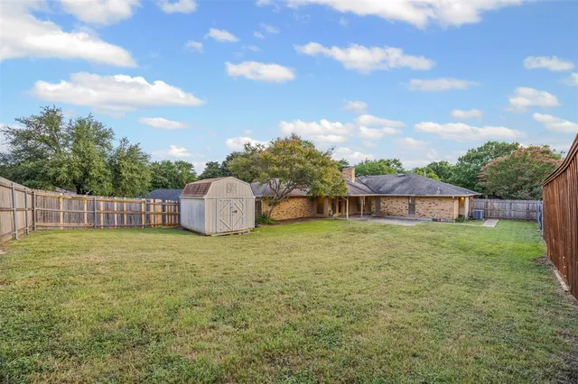 a tall yellow building sitting in a big yard with large trees