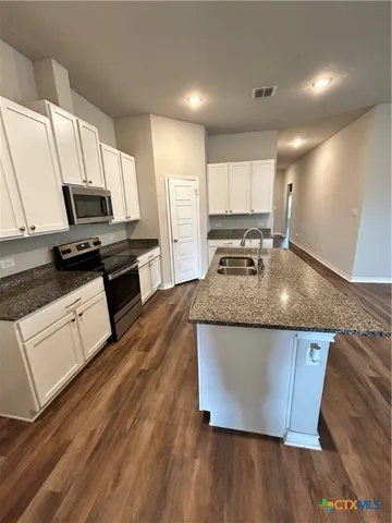 a kitchen with kitchen island granite countertop a stove top oven a sink a counter space and cabinets