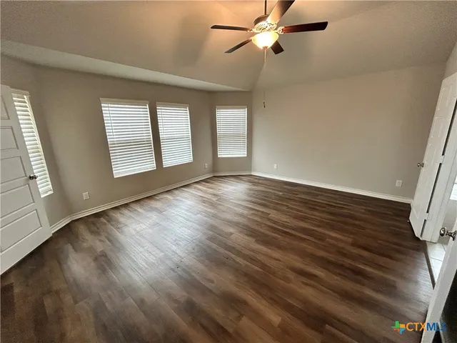 an empty room with wooden floor fan and windows