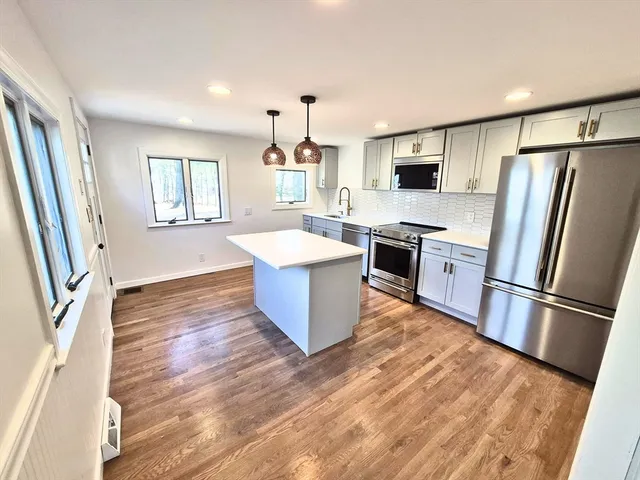 a large kitchen with stainless steel appliances granite countertop a stove a sink dishwasher a refrigerator and a stove with wooden floors