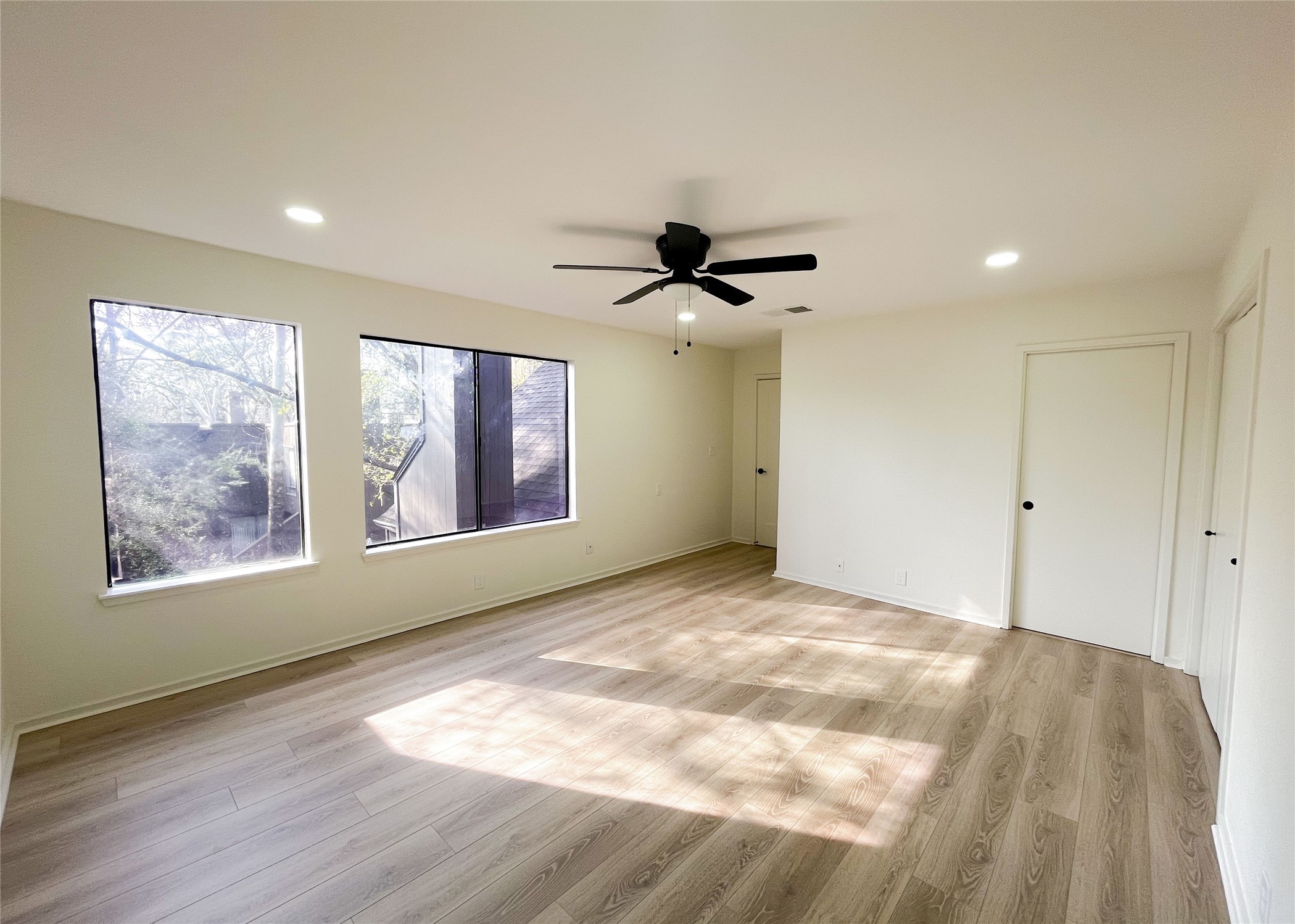 238 Litchfield Lane Houston, TX 77024 - Photo 12 of 25 Experience the spacious primary bedroom featuring light wood floors, abundant natural light, and a modern ceiling fan. Enjoy recessed lighting and ample storage with sleek white sliding closet doors.
